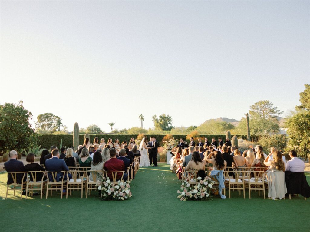 Outdoor wedding ceremony at Andaz resort with guests seated and bride and groom standing at front of ceremony altar space holding hands.