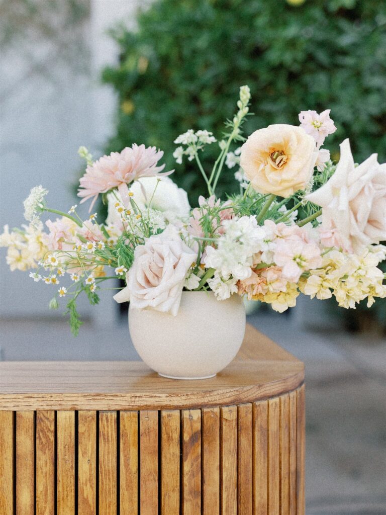 Wedding floral arrangement of pink, white, yellow and peach flowers in neutral vase.