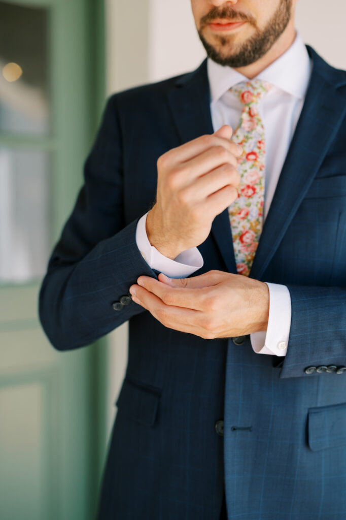 Groom buttoning cuffs of blue jacket suit.