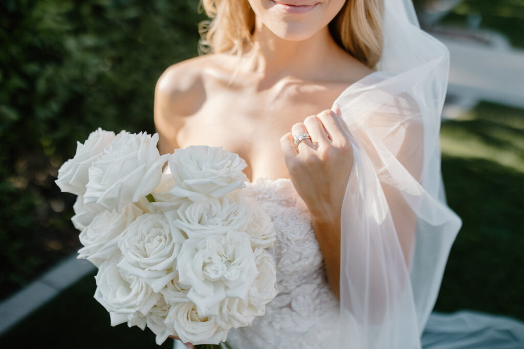 Bride holding white roses bouquet and veil in other hand.