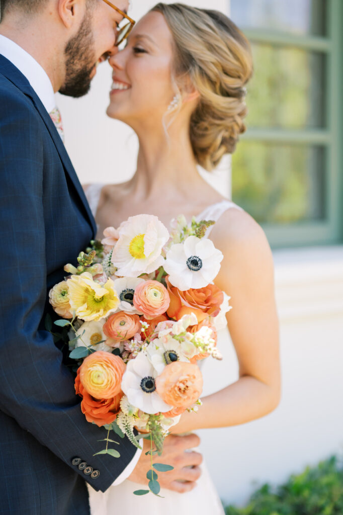 Bride and groom touching noses together, smiling, bride holding bouquet.