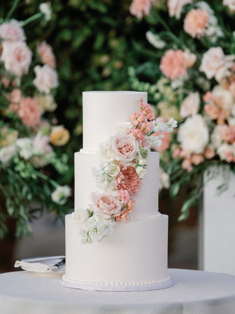 Three tiered white wedding cake with pink and white floral added in diagonal line up the front.