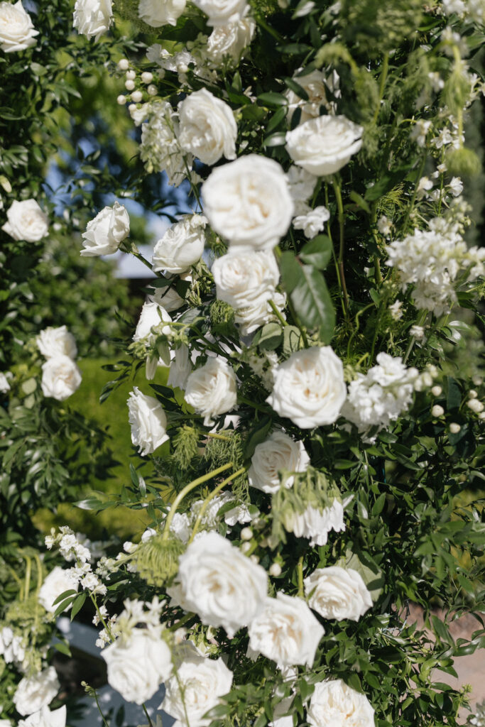 Details image of white flowers and greenery on wedding ceremony pillars.