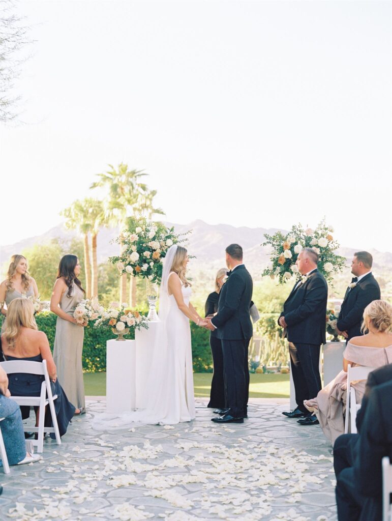 Bride and groom holding hands at altar space in outdoor wedding ceremony.