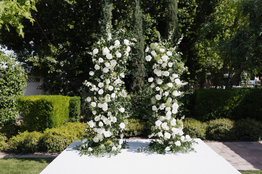 Two floral pillars for wedding ceremony altar space of white flowers and greenery.