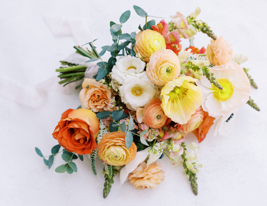 Bridal bouquet of white, yellow, peach, pink, and orange flowers.