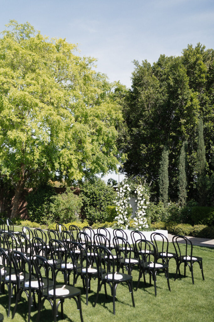 Outdoor wedding ceremony at Stonebridge Manor with black chairs and white floral and greenery floral pillars in altar space.