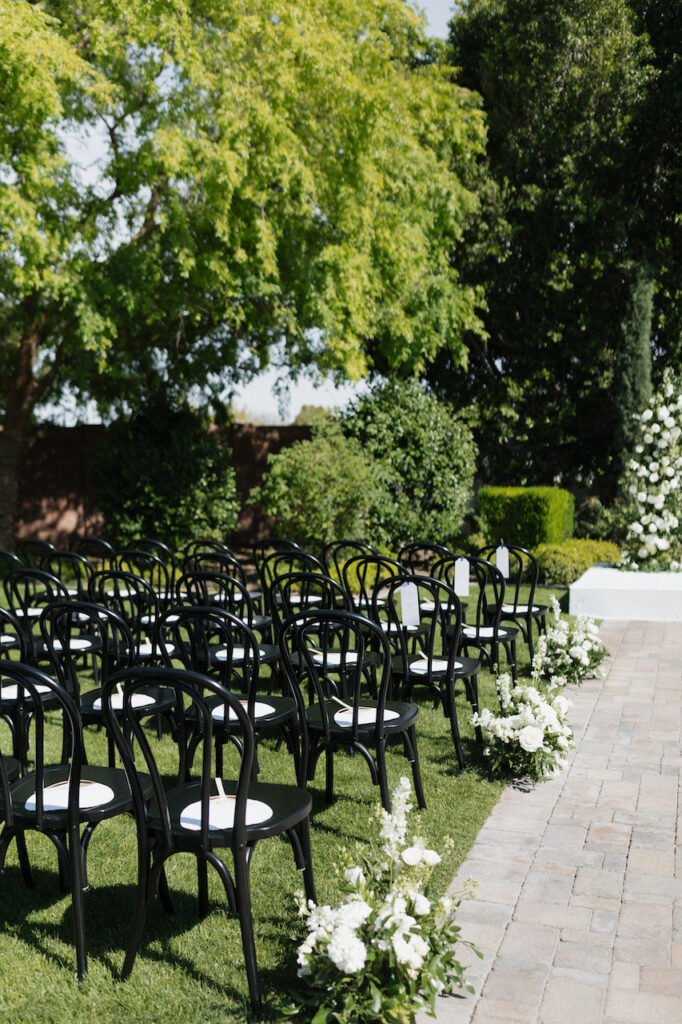 Outdoor wedding ceremony at Stonebridge Manor with black chairs and white ground aisle floral.