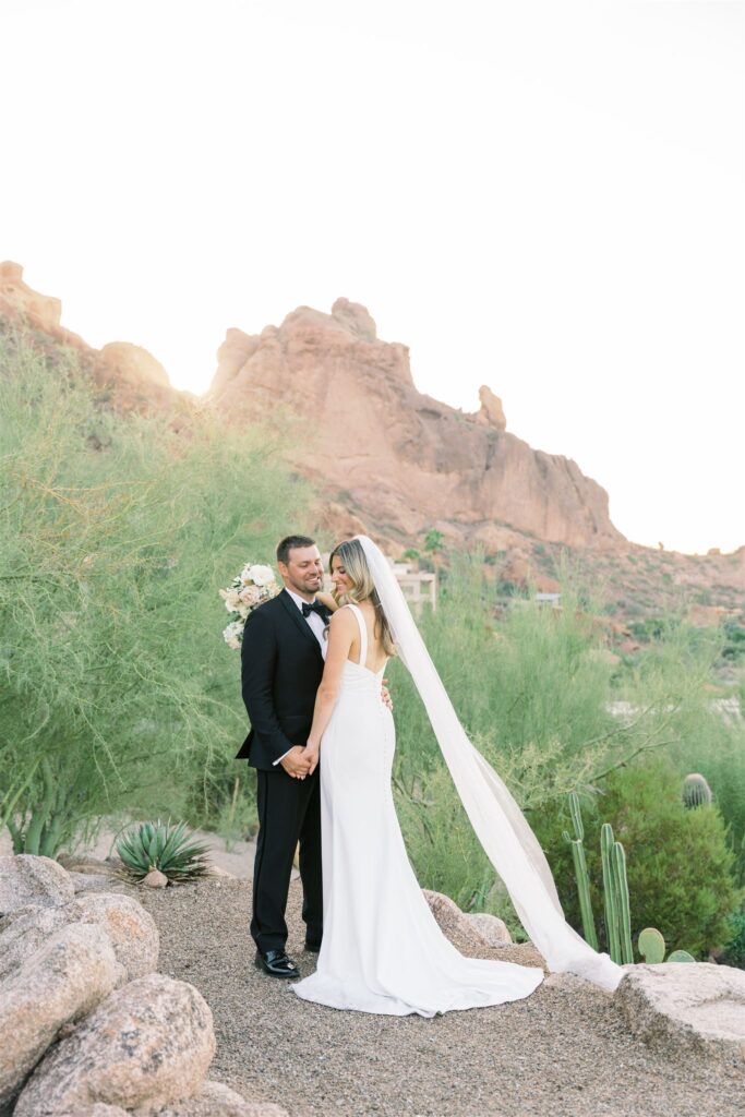 Bride and groom embracing standing in desert landscape.