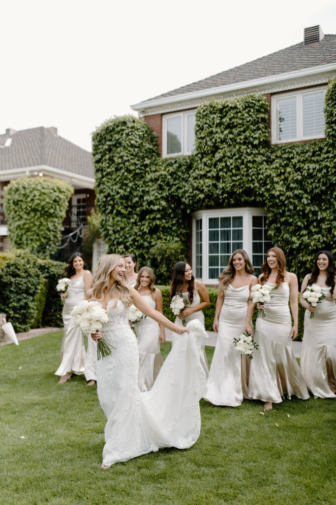 Bride walking in front of bridesmaids in cream colored dresses holding white flowers bouquets.