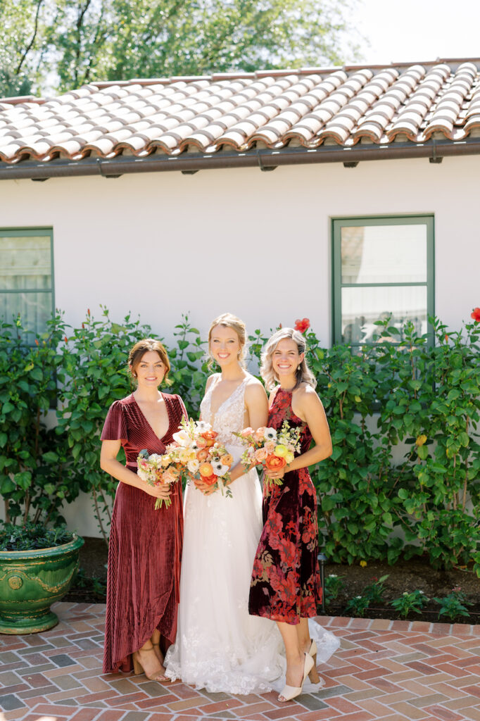 Bride standing between two bridesmaids in red dresses, all holding bouquets.