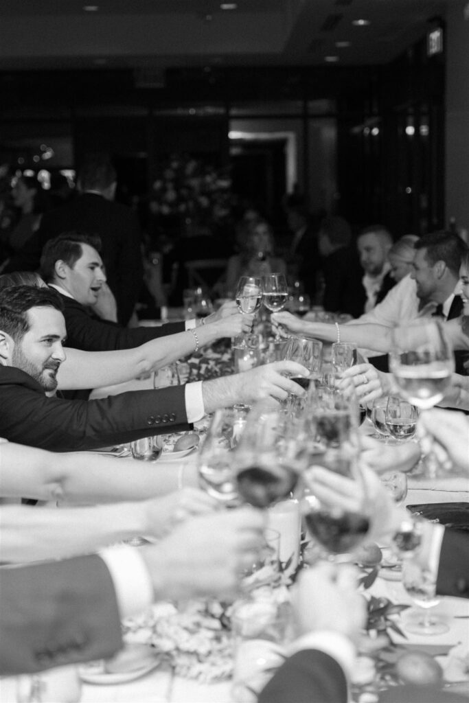 Guests toasting glasses at long wedding reception table.