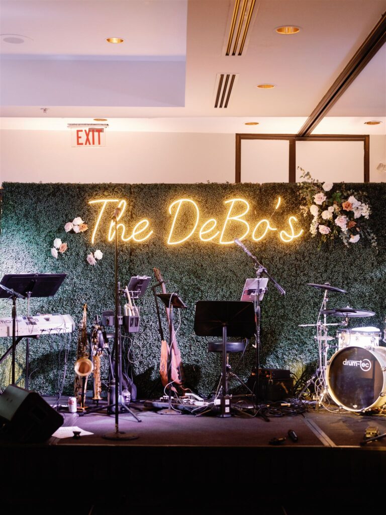 Wedding reception band stage with greenery wall behind with neon sign and floral attached.