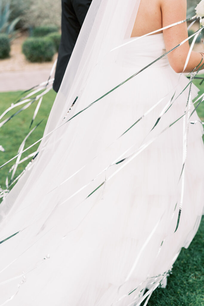 Side of bride with veil trailing behind her and long silver streamers off to her side.