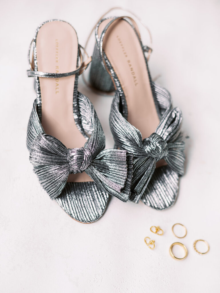 Metallic silver bridal wedding shoes with earrings and rings off to side.