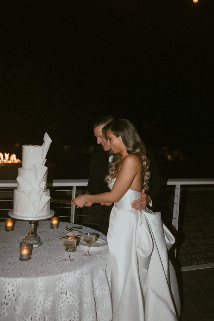 Bride and groom cutting three tiered white wedding cake with folds added to outside.