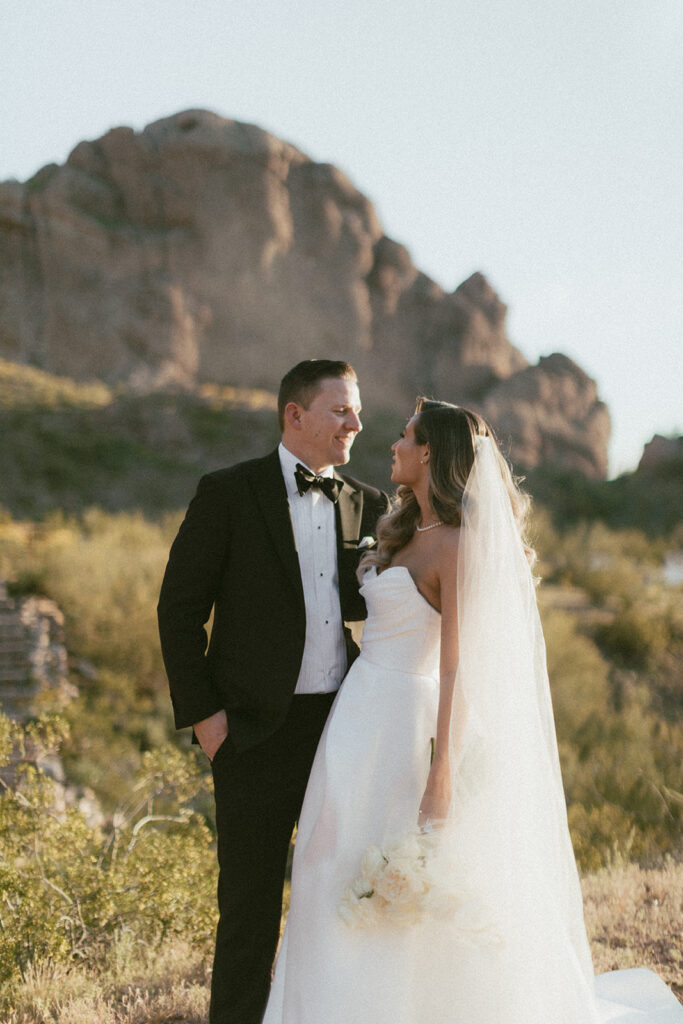 Bride and groom with one arm around each other looking into each other's faces with Camelback Mountain in background.