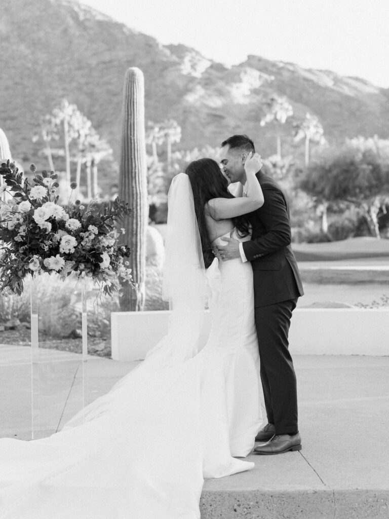 Bride and groom kissing in front of desert landscape with mountain in the back.