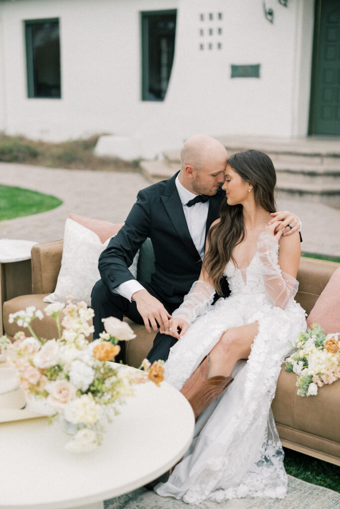 Bride and groom resting foreheads together while seated on a couch outside.