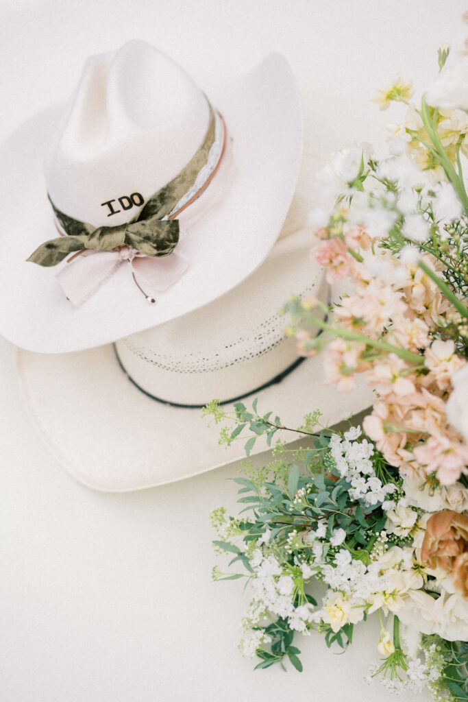 Bride and groom cowboy hats on top of each other, placed next to a bouquet of flowers.