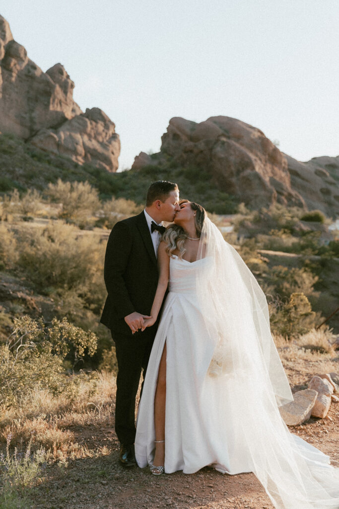 Bride and groom kissing and holding hands with Camelback Mountain in background.