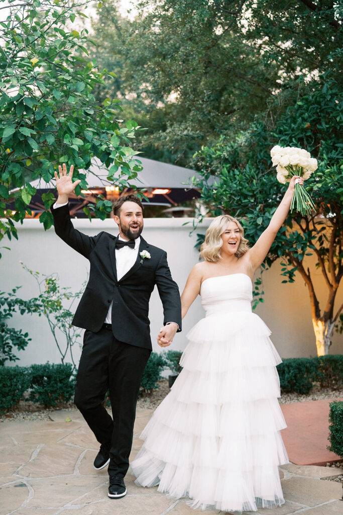 Bride and groom walking holding hands and smiling with their outside hands raised in celebration.