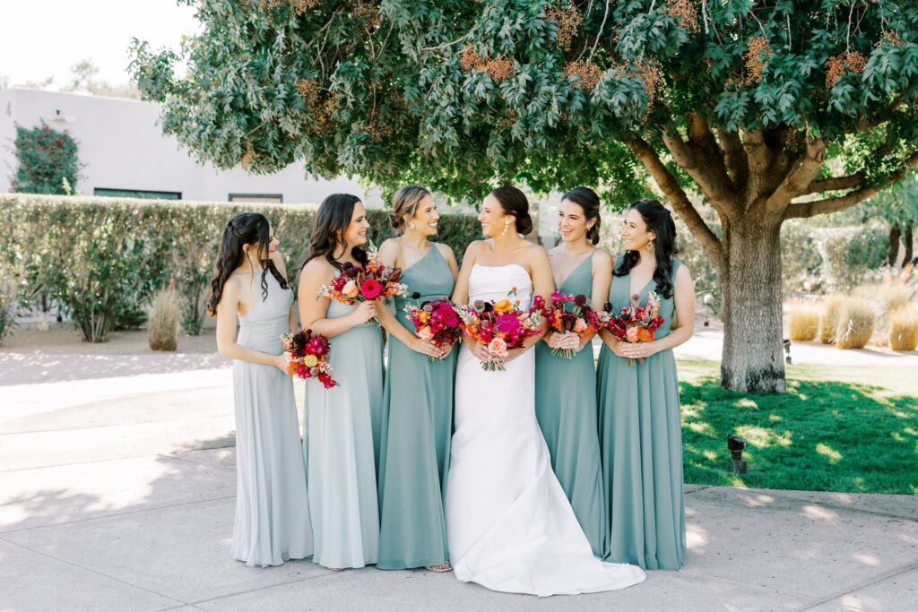 Bridesmaids standing in a line under a tree with bride all holding bouquets and smiling.