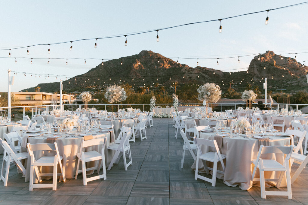 Outdoor Mountain Shadows wedding reception on patio with round tables with high and low centerpieces of white flowers.