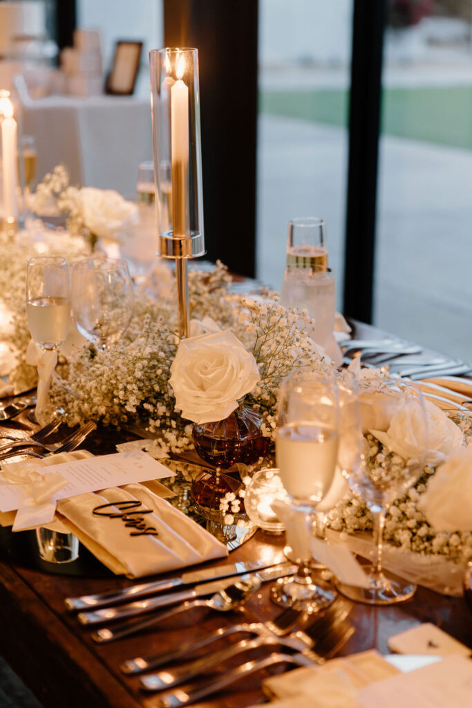 Long reception table decor with white taper candles, baby's breath, and white roses.