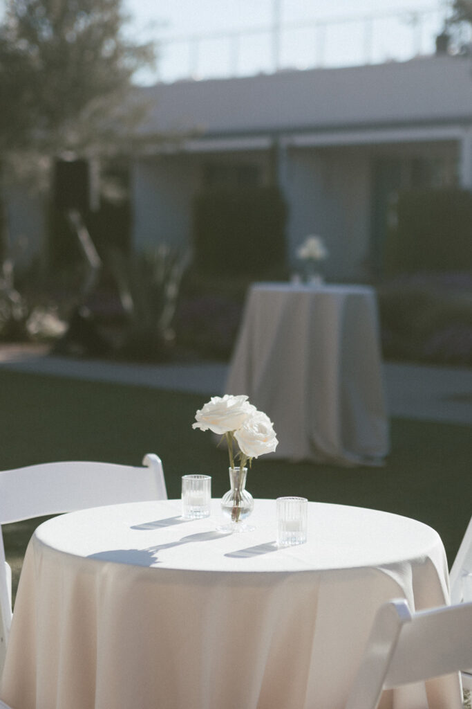 High boy cocktail hour tables with white roses in bud vases with votive candles on top.