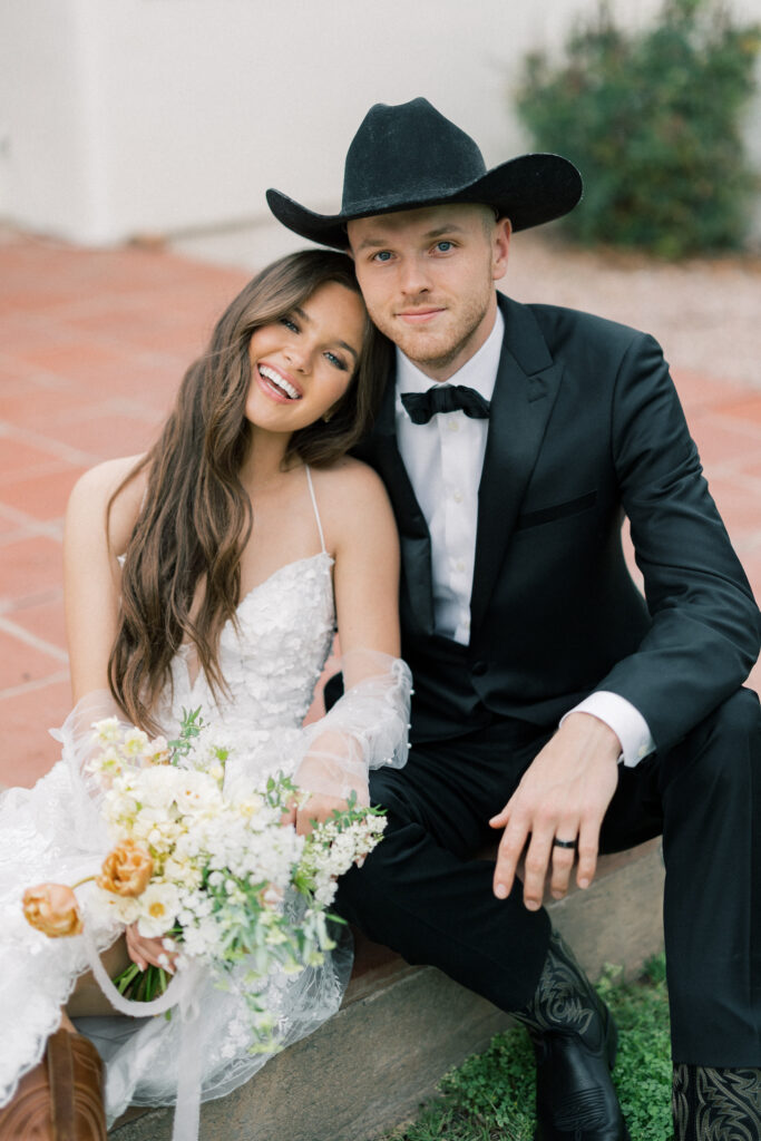 Bride resting head on groom wearing a cowboy hat, shoulder. Bride holding bouquet.