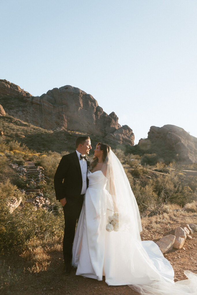 Bride and groom with one arm around each other looking into each other's faces with Camelback Mountain in background.