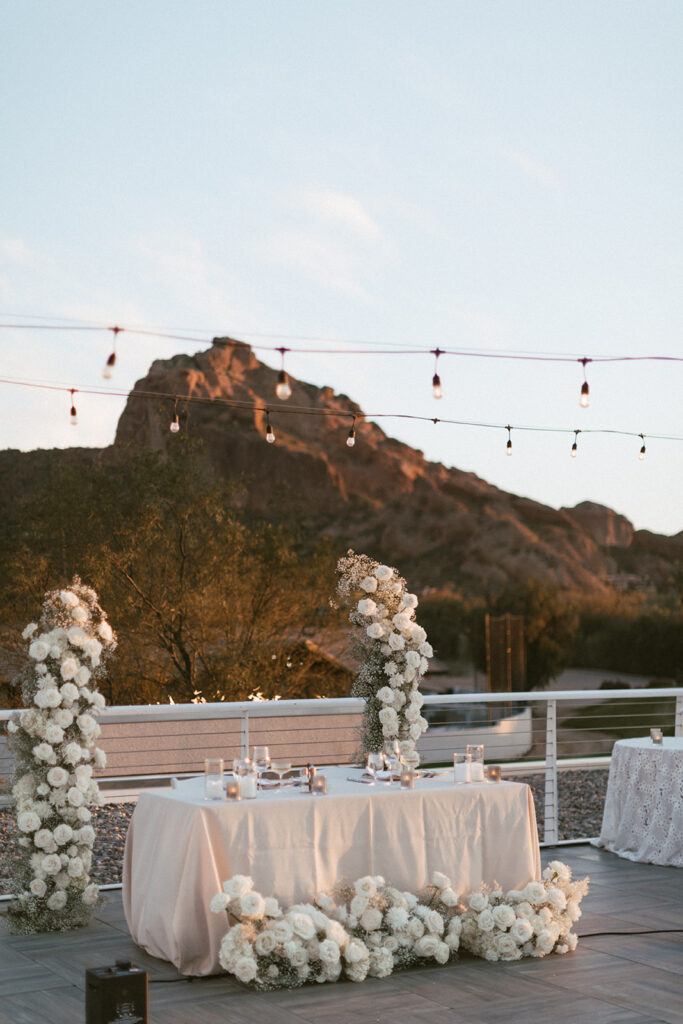 Outdoor patio reception sweetheart table with floral columns behind it and ground floral in front of it.