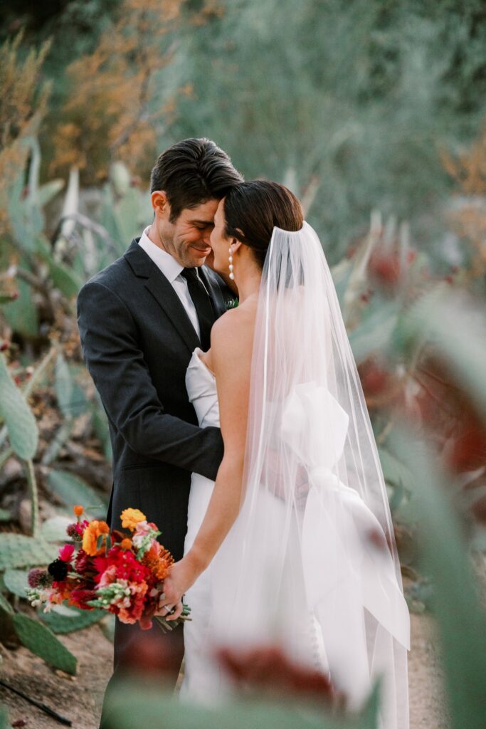 Bride and groom embracing with foreheads touching in desert landscape.