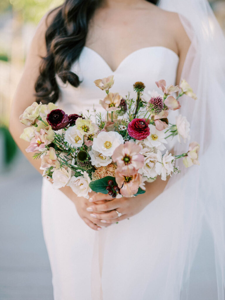 Bridal bouquet of white, pink, blush, and maroon flowers held by bride.