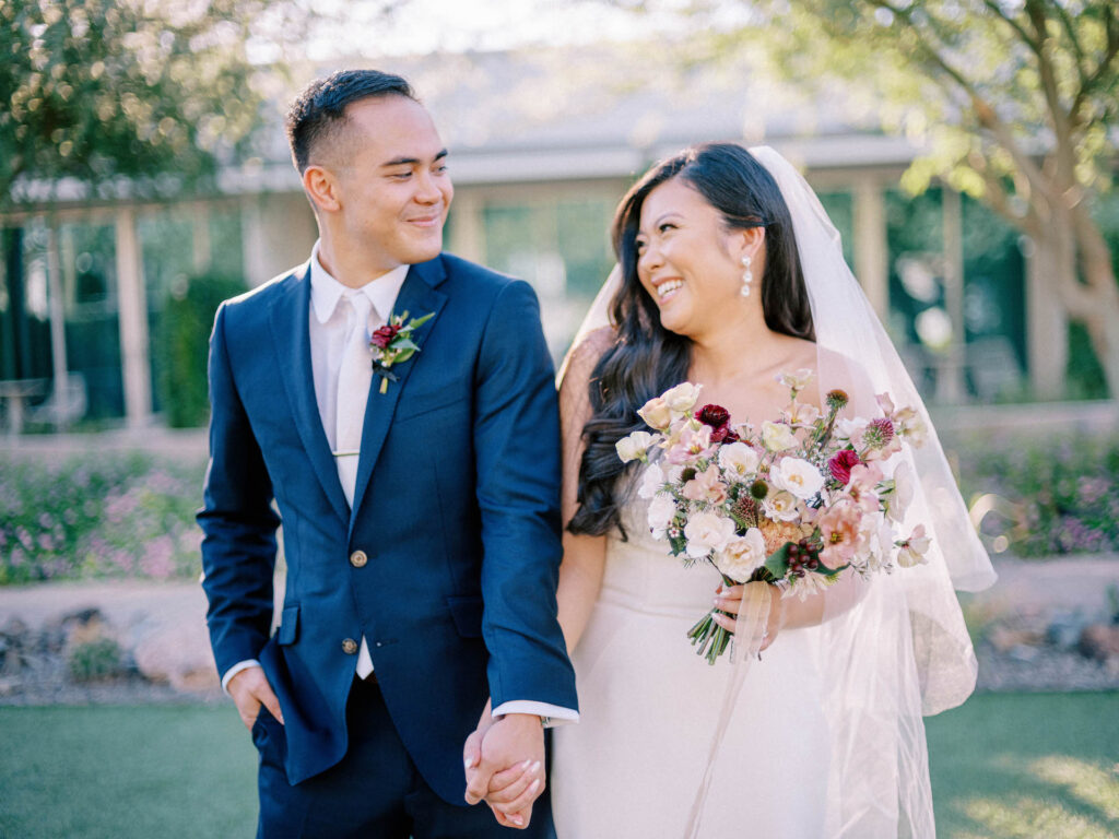 Bride and groom holding hands and smiling at each other.