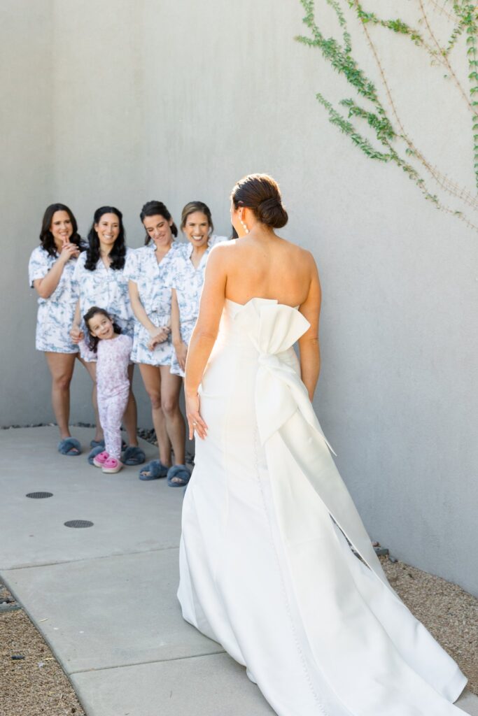 Bride showing bridesmaids wearing pajamas her dress for the first look.