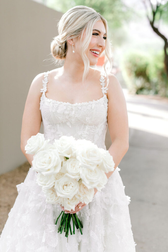 Bride smiling off to side holding white long stem roses bouquet.
