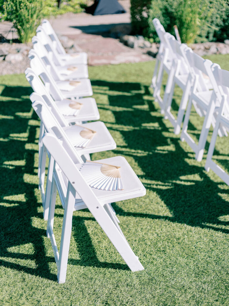 White wedding ceremony folding chairs with white fans placed on them.