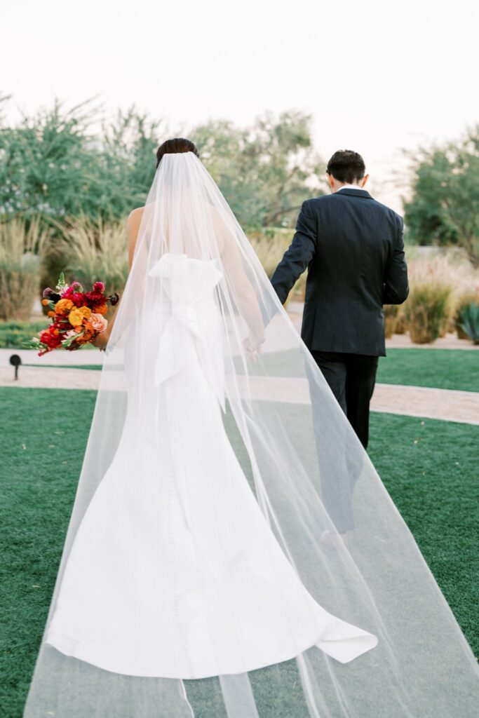 Bride and groom walking away in grass, holding hands.