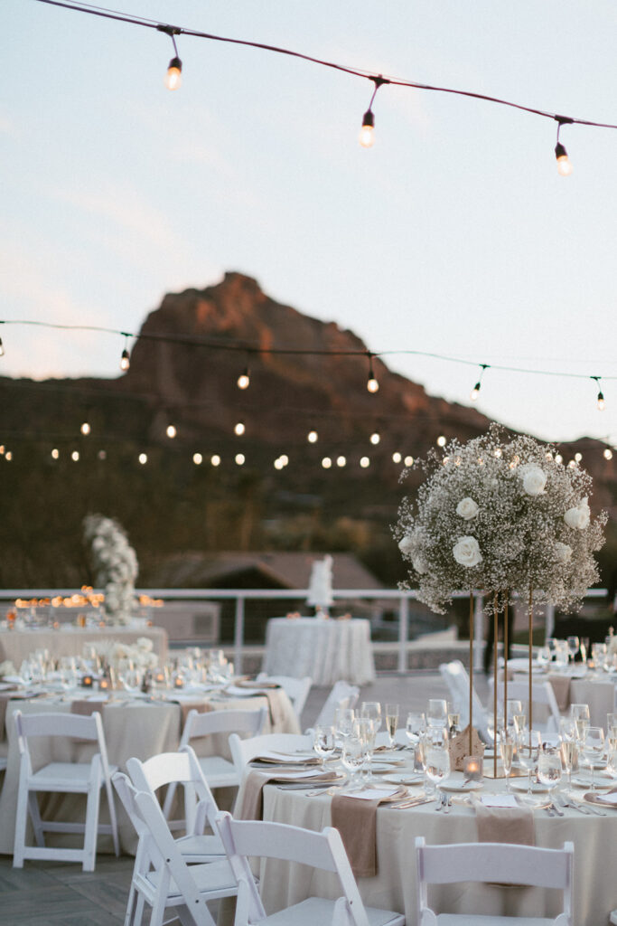 Outdoor Mountain Shadows wedding reception on patio with round tables with high and low centerpieces of white flowers.