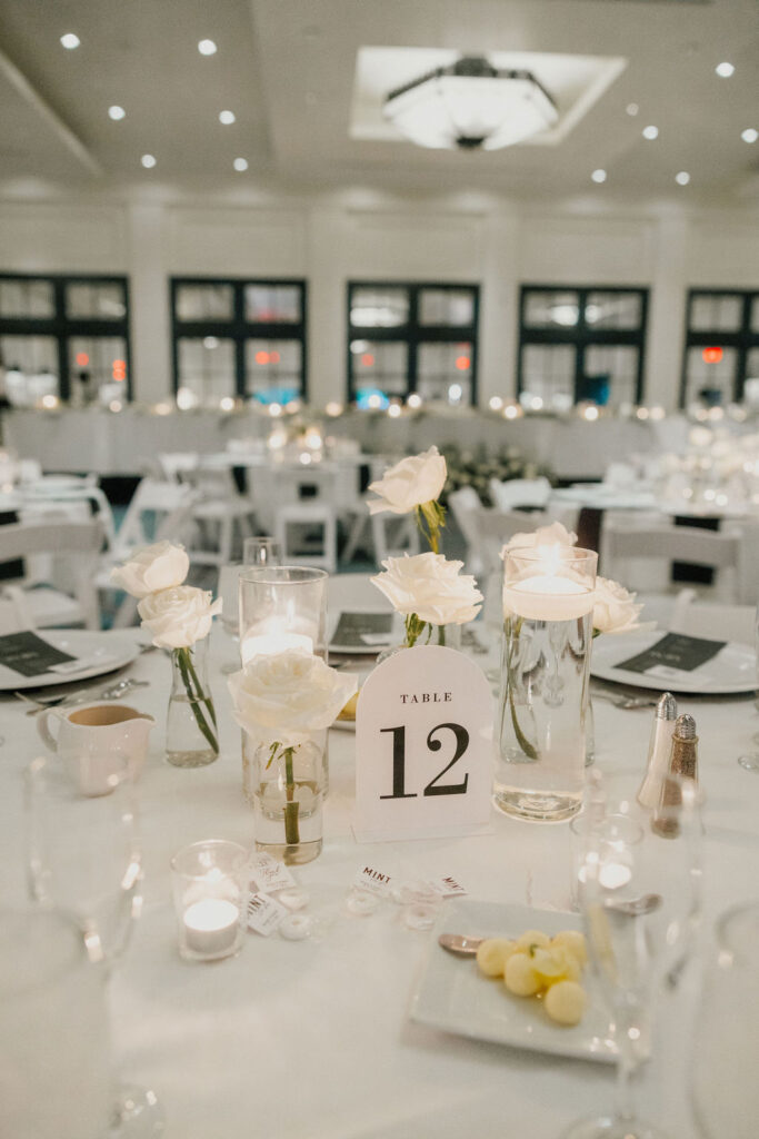 Reception centerpieces of white roses in bud vases and floating candles.