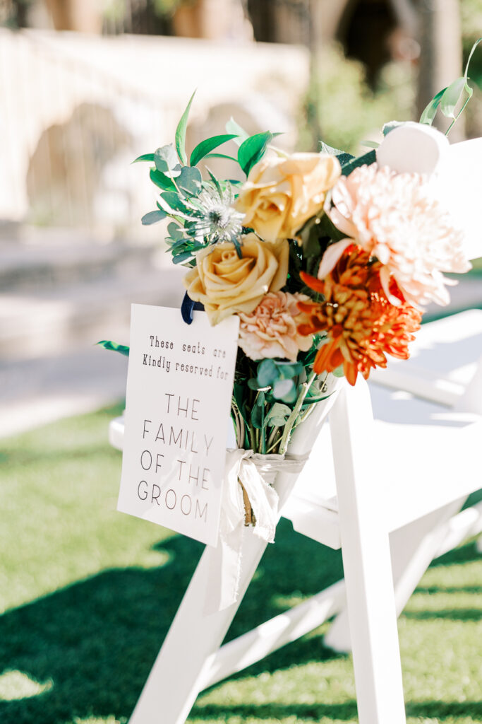 Wedding reception white chair with floral added to outside aisle side and sign noting chairs are for the family of the groom.