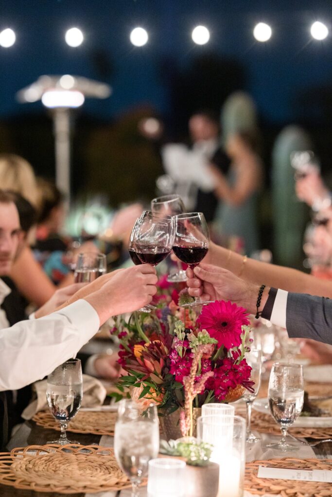 Guests toasting wine glasses across table at wedding reception.