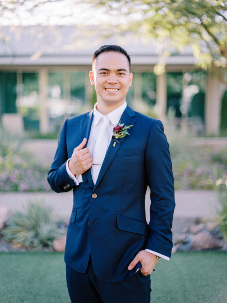 Groom standing and smiling, holding onto lapel.