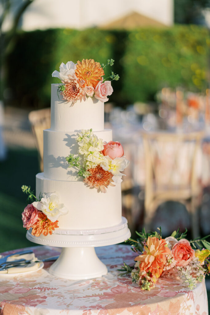 Three tiered white wedding cake with flowers added in pink and orange colors.