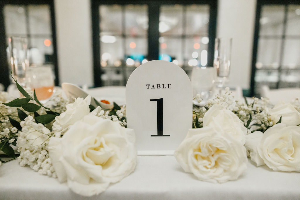 Wedding reception table number decor of white flowers around it.