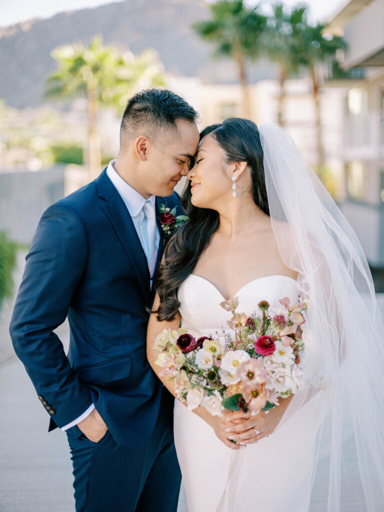 Bride and groom smiling and resting their foreheads together with bride holding bouquet.