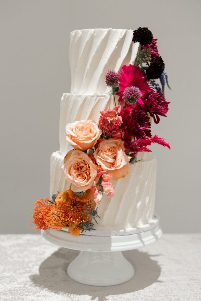 Three tiered white wedding cake with ombre floral design added in arch across front from bottom to top.