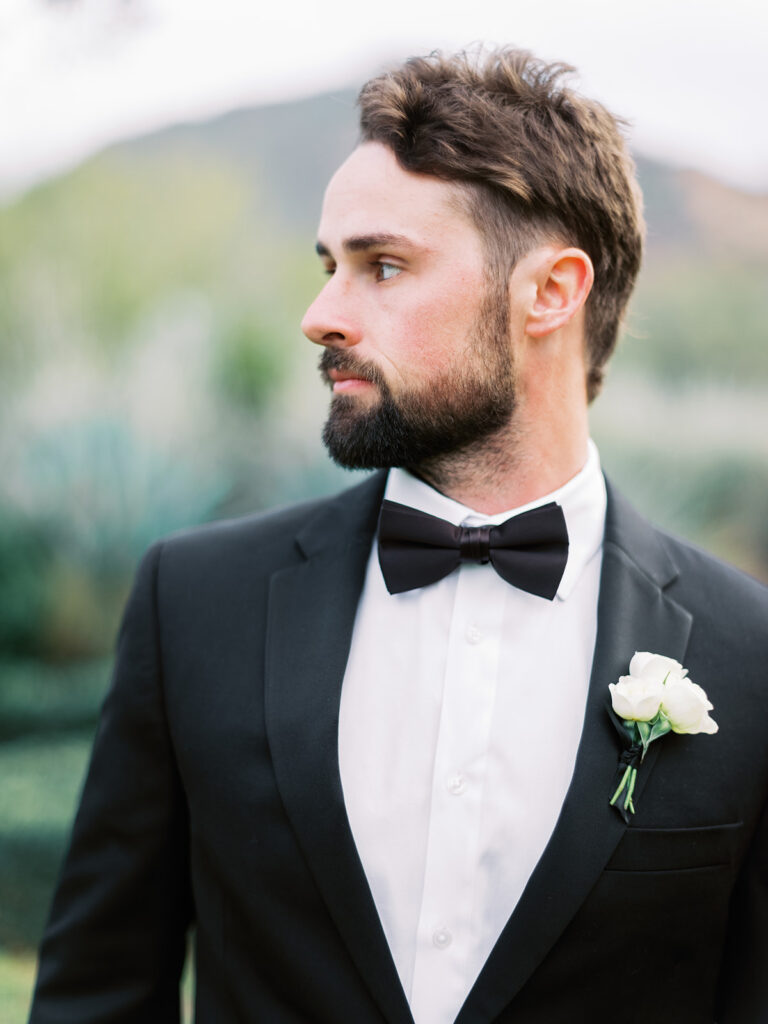 Groom in black tux and white roses boutonniere looking off to side.